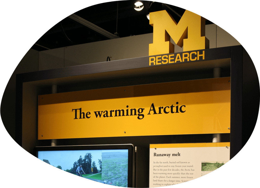 A photo of a museum display featuring a large digital screen. The exhibit title reads "M Research: The warming Arctic"