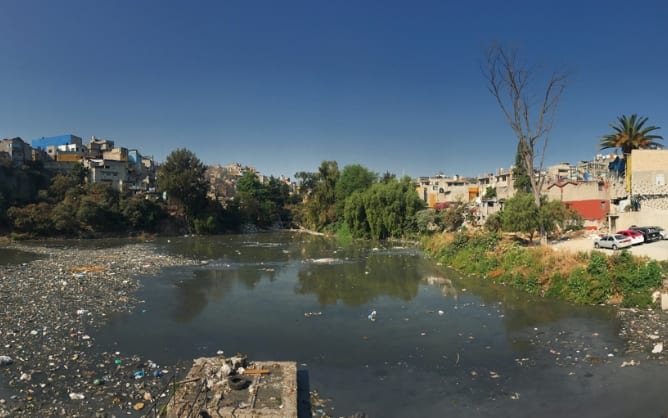 A photo of a river strewn with debris in a highly populated area.