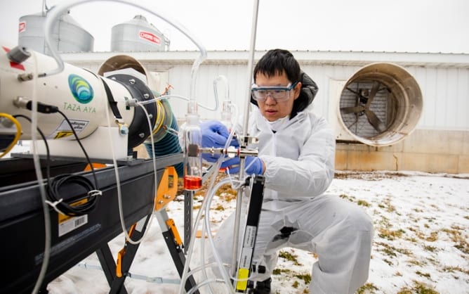 A person in a protective gown and safety goggles operates a testing apparatus outdoors in snow.
